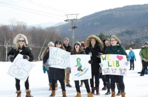 Friends cheer on post author and Clarkson student Libby McCusker at her last home race, holding celebratory signs in the snow.