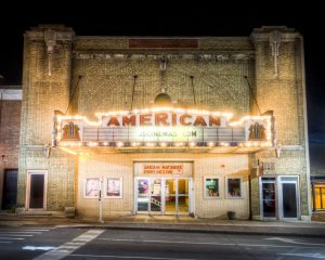 A brick building that is light up at night with the marquee that reads American