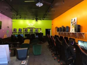 A multi colored room with orange, green, and pink walls that ve computers lining the entire wall with big chairs