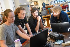 Four students gather around a laptop. 