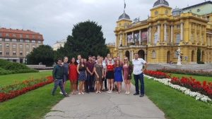 A group of people standing on a path that leads through a garden with a big yellow building in the back
