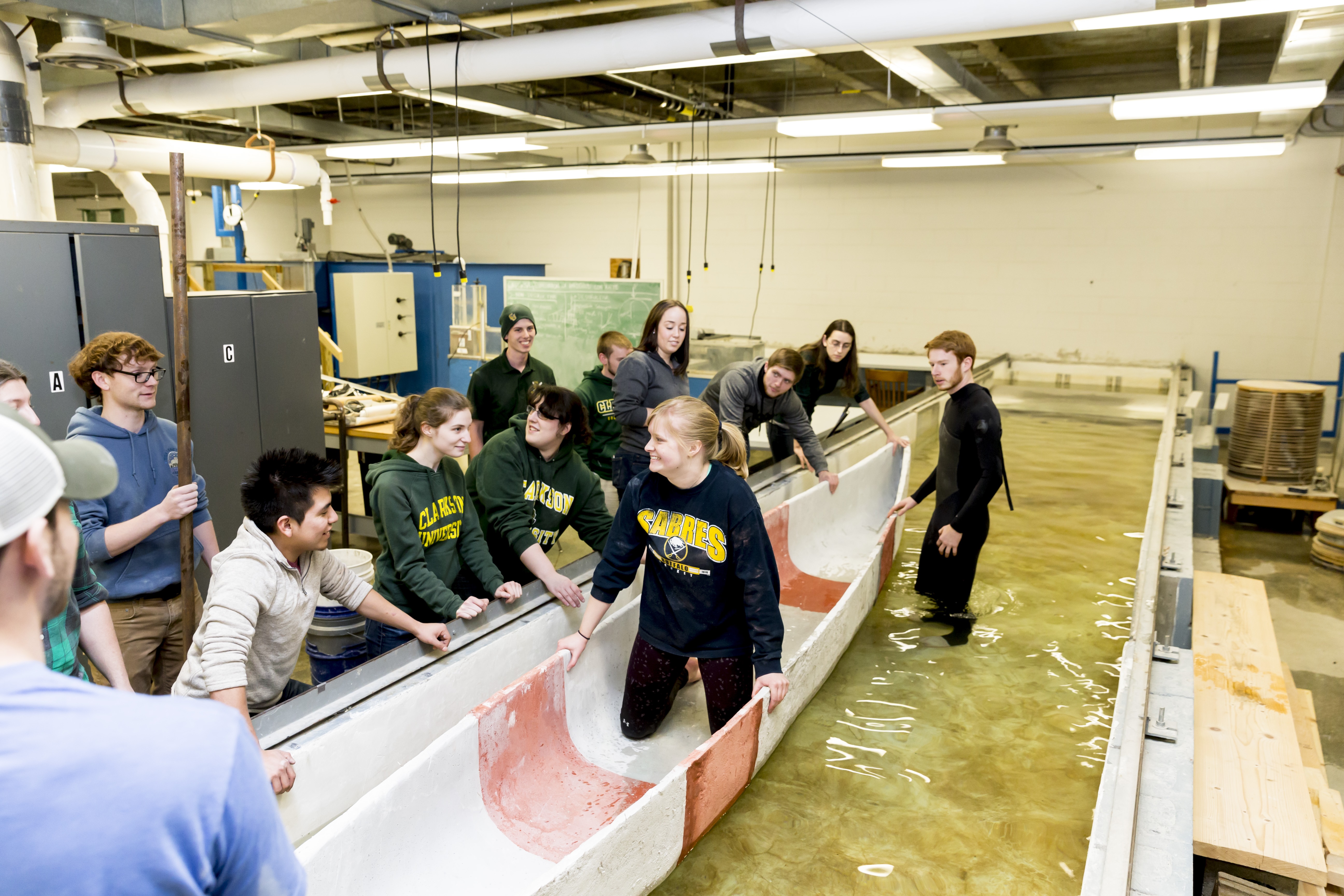 Students sitting in the concrete canoe that is in a water bath