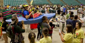 Groups of students from various Clarkson student clubs, including some hoisting and sitting in a kayak, display their clubs during Clarkson's annual Spring Accepted Students Days in Cheel Arena.