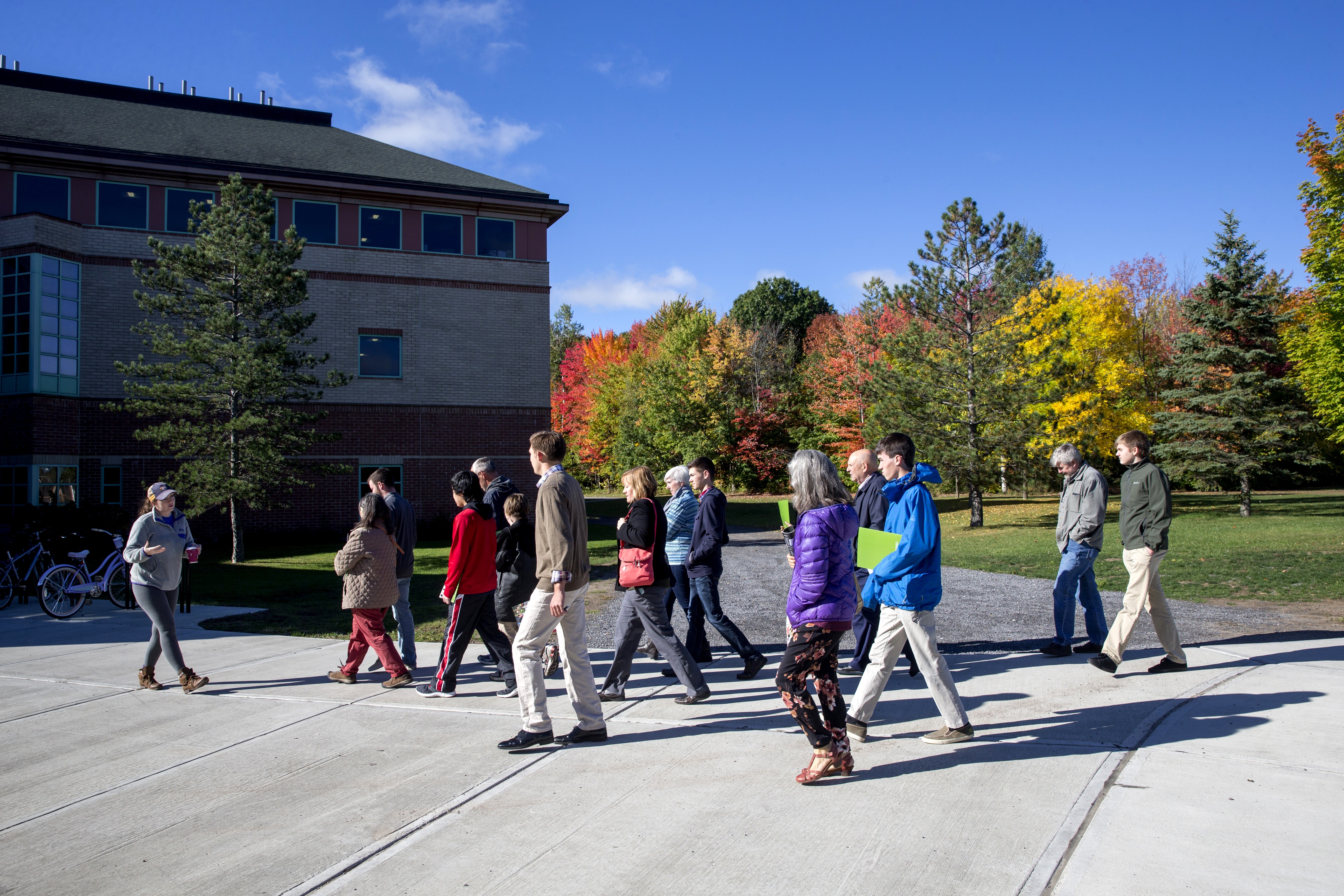 A group of students walking along a path with a building in the background and colorful trees of red, green, and yellow
