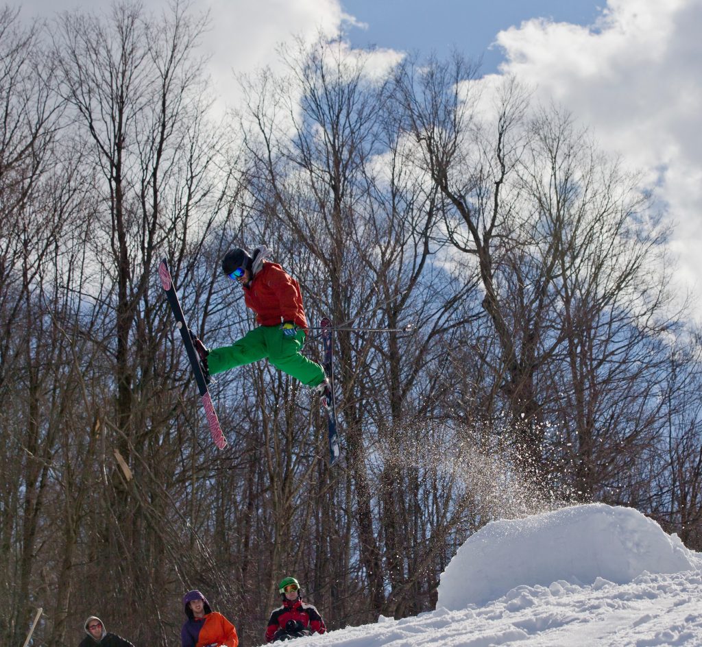 A person in green pants ski jumping off a snow pile