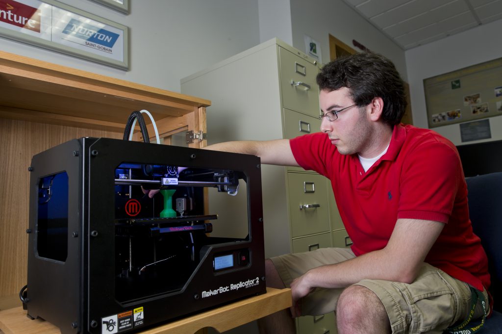 A man sitting next to a 3D printer