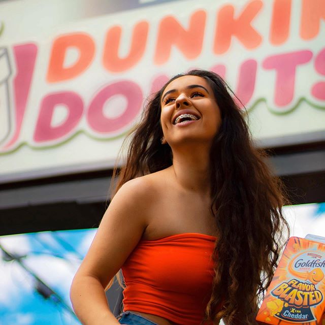 A model has her photo taken holding a box of Goldfish in front of a Dunkin' Donuts by Clarkson student Jada Flanagan in downtown Potsdam, New York. 