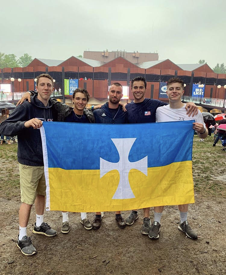 Sigma Chi Brothers standing holding their blue and gold flag
