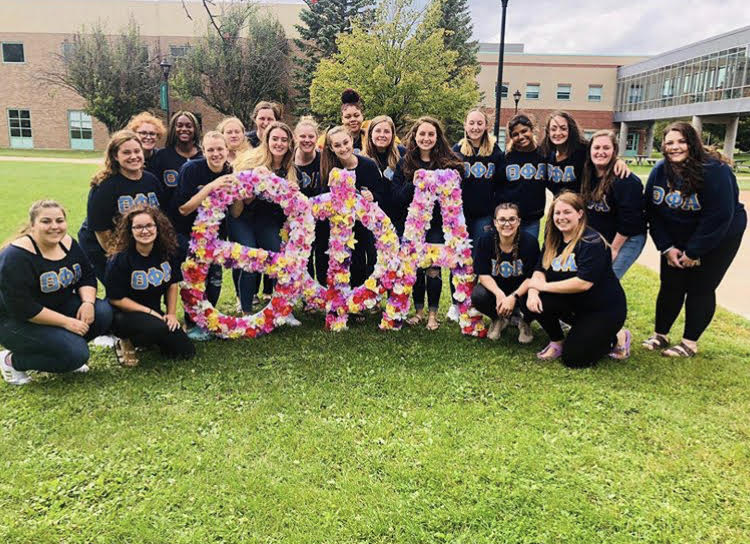 A group of Theta Phi Alpha sorority sisters posing behind flowery letters on Cheel lawn
