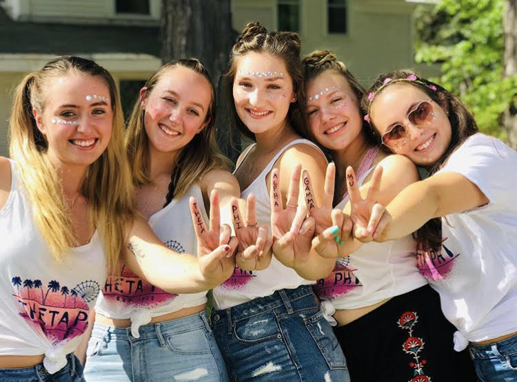 Sisters of theta phi holding up a peace sign, with 'Theta phi' written on their hands