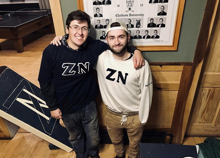 Two Zeta Nu Fraternity brothers standing in front of a composite photo