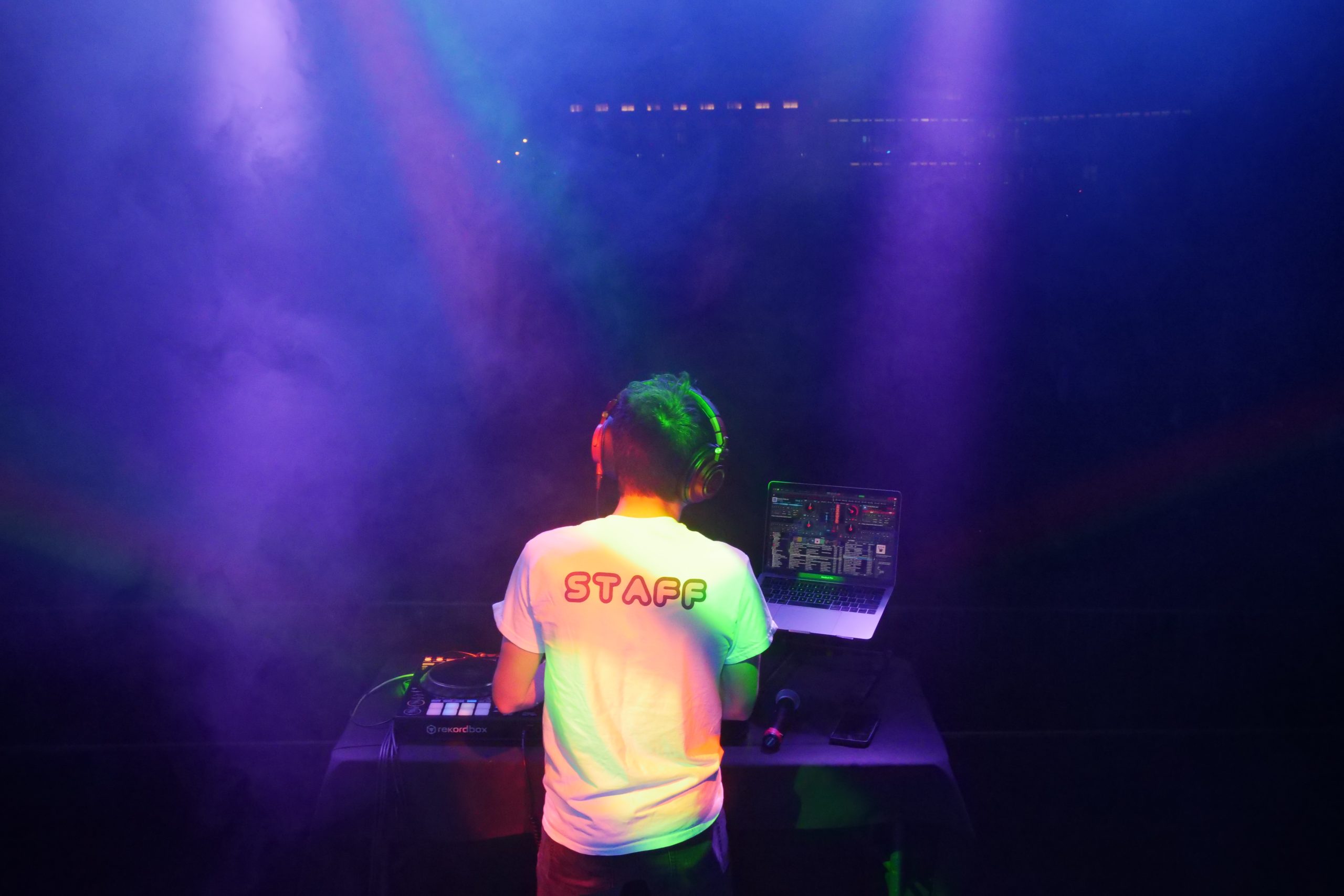 Photo of Caleb DeLaBruere DJing on a stage with colored light