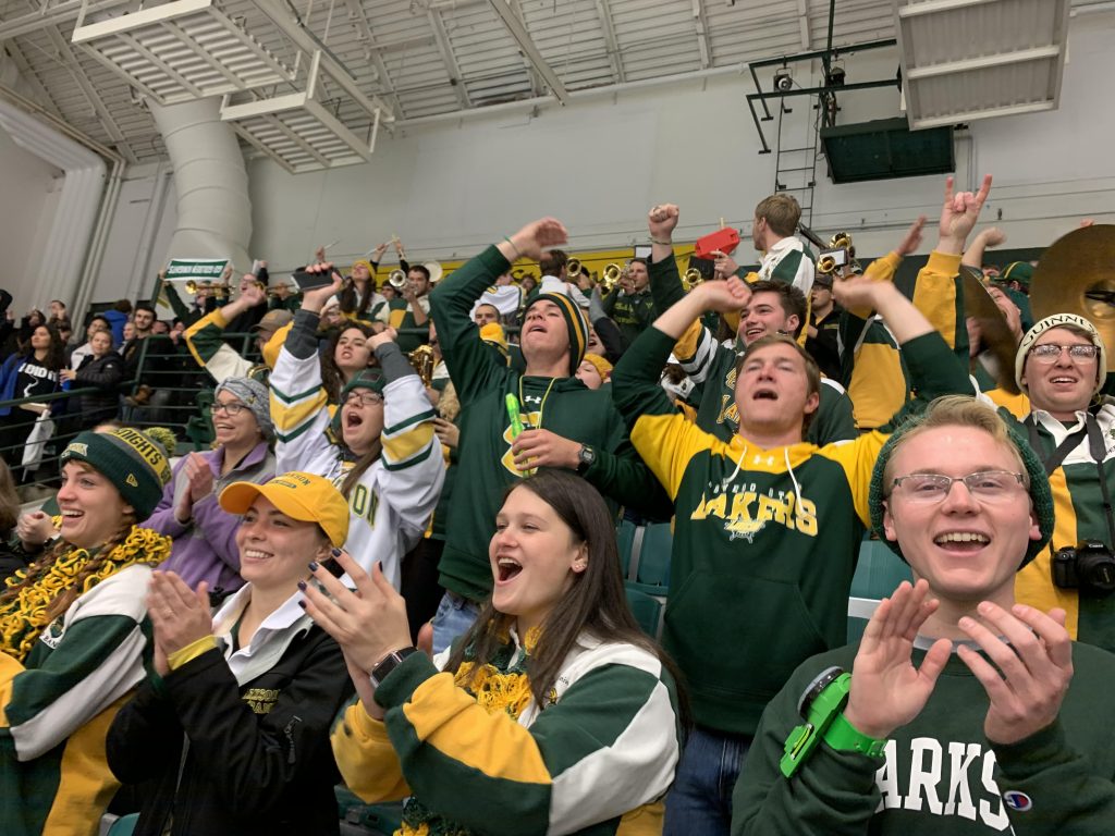 A crowd of the Clarkson University Pep Band cheers on Golden Knights hockey at Cheel Arena in the student section.