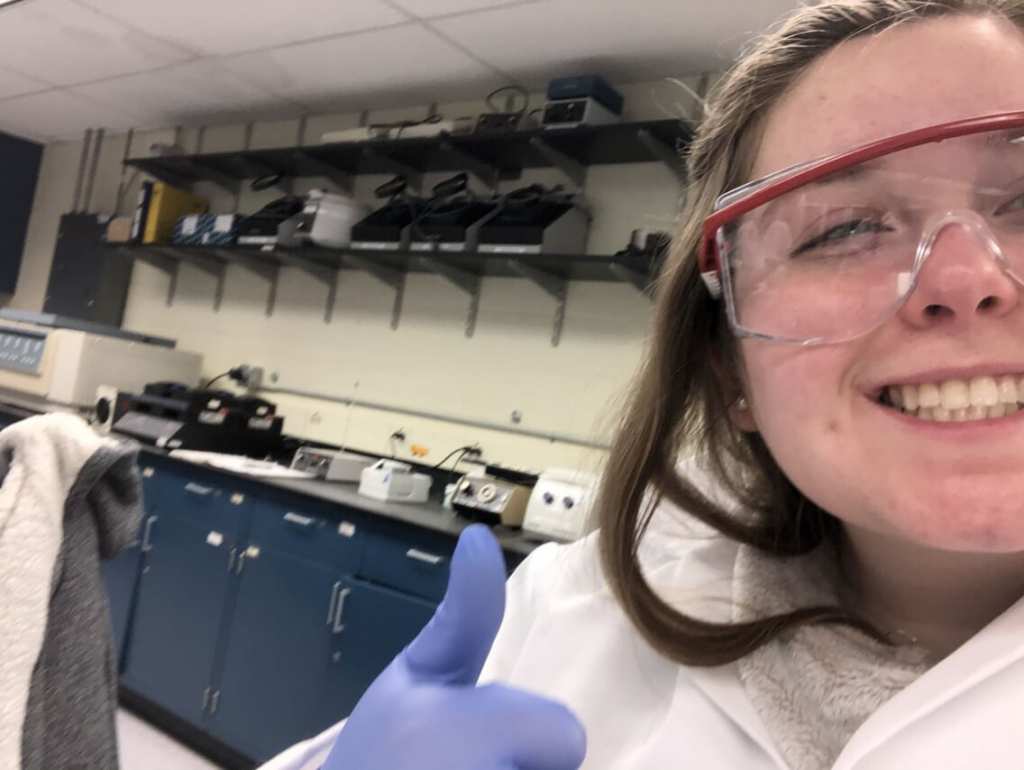 Megan taking a seflie in a lab coat working in the Biochem Biotech lab at Clarkson