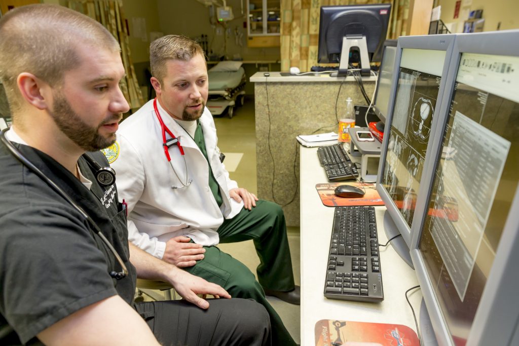 Physician Assistant student Aaron Cooper sits with a hospital employee at a computer while completing his rounds.
