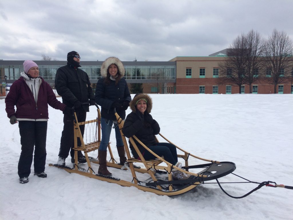 Jennifer Karekos '14 sits on a dog sled outside with three other people while back at Clarkson's campus for Cold Out Gold Out.