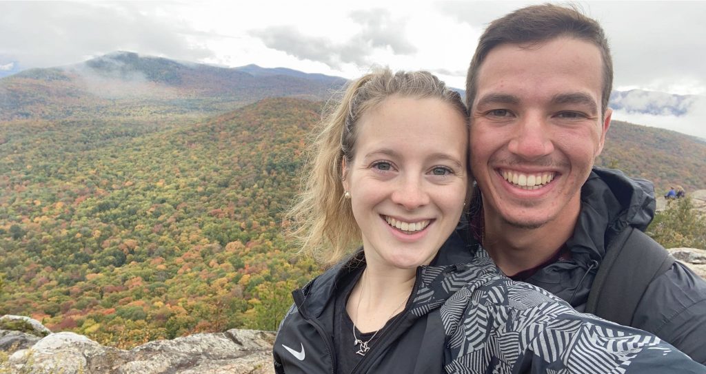 A couple smiling into the camera with a mountain range as the backdrop 