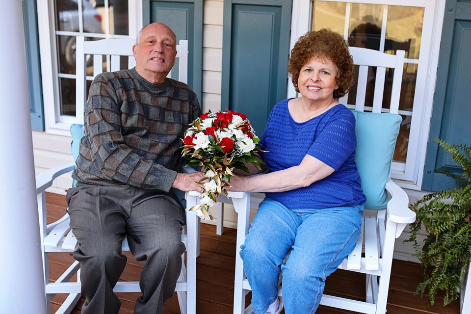 Two people sitting in a rocking chair holding a red and white flowers