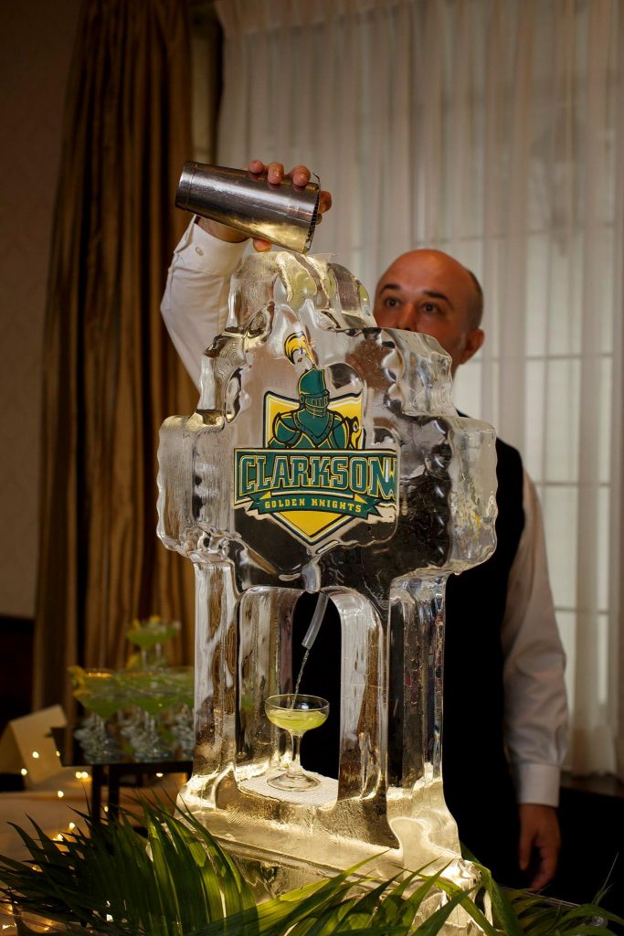 A man pours a drink into an ice sculpture with Clarkson's logo on it.