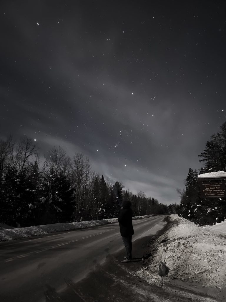 person standing next to dark Adirondack road starry night