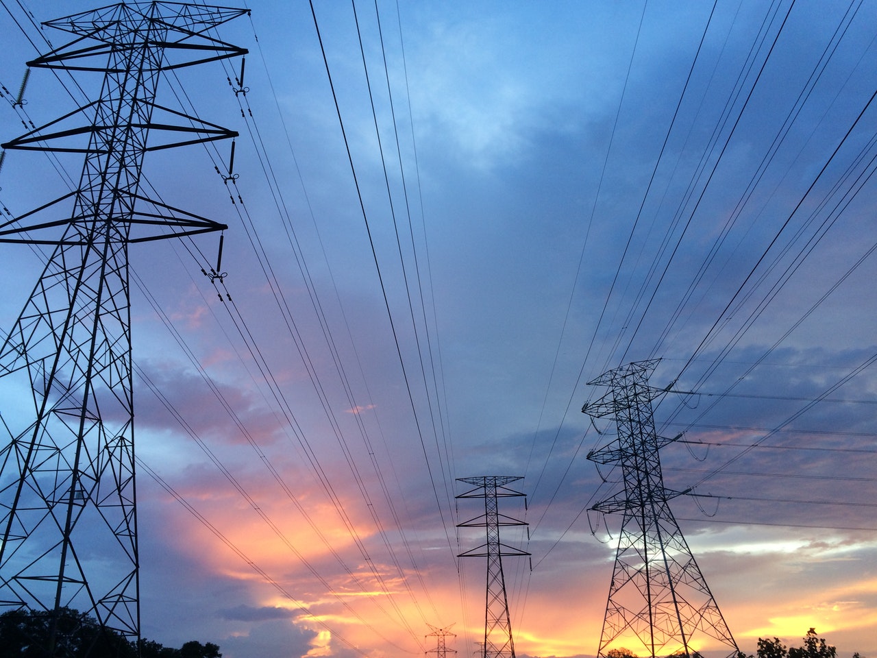 An outdoor image of power lines and electricity towers in the sunrise lit sky.