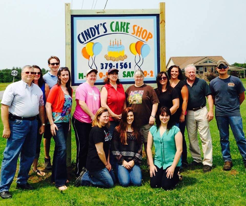 A photo of the staff at Cindy's Cake Shop in Canton, New York in front of the business' sign.