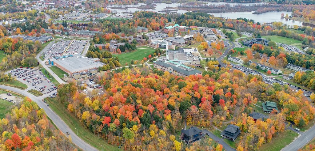 Aerial view of the whole campus of Clarkson with fall foliage and the Racquette river in the background