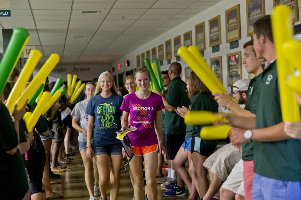 First-year students walking through a parade with their peers cheering them on.