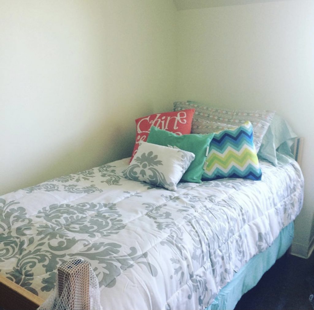 A bed in a dorm room with decorative pillows 
