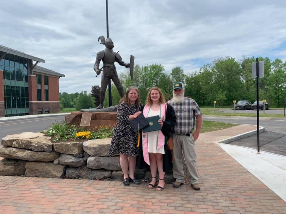 Megan Parkman holding her diploma, standing with her parents in front of the Clarkson Golden Knights Statue