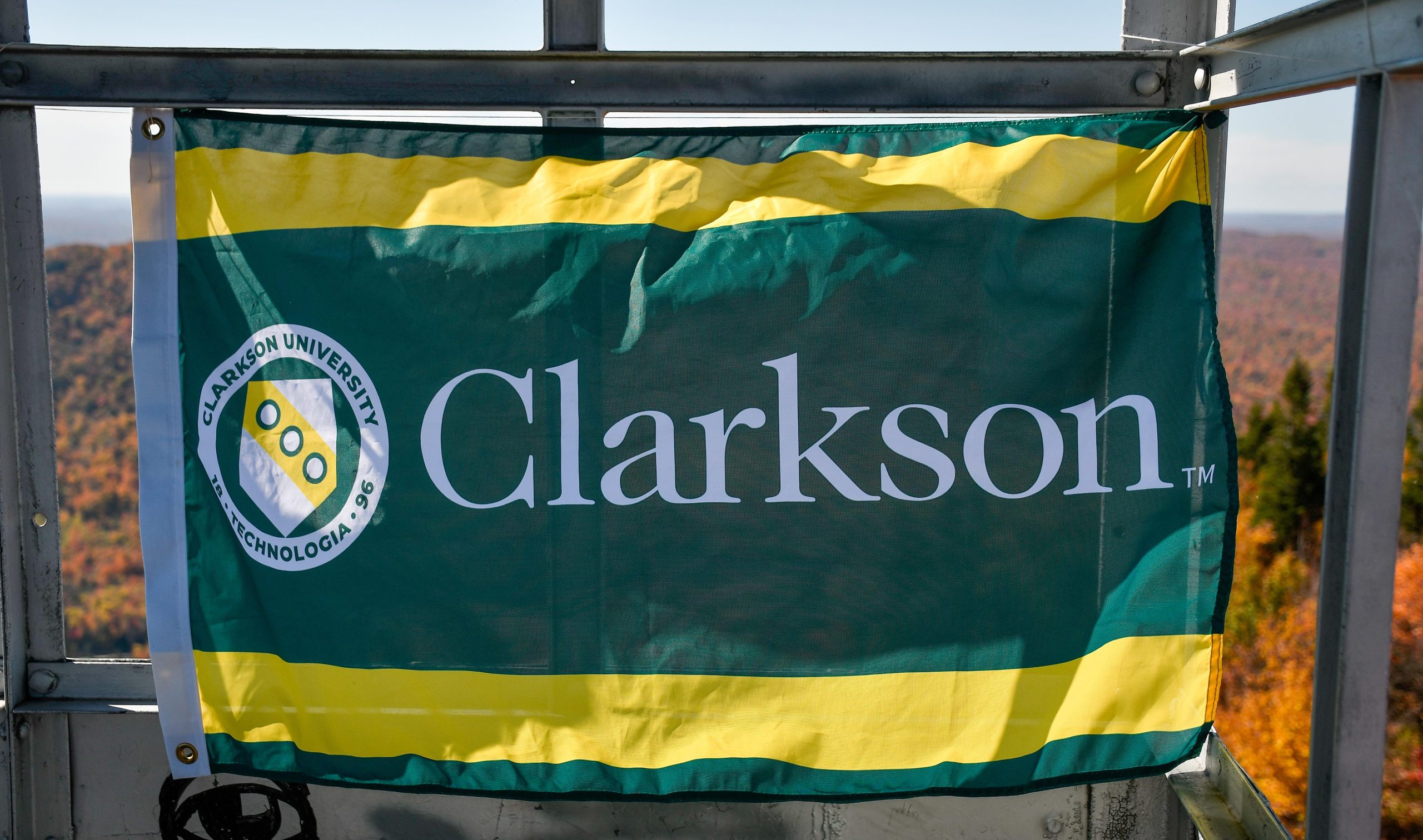 A Clarkson University flag displayed on the top of an Adirondack Mountain in the fall.