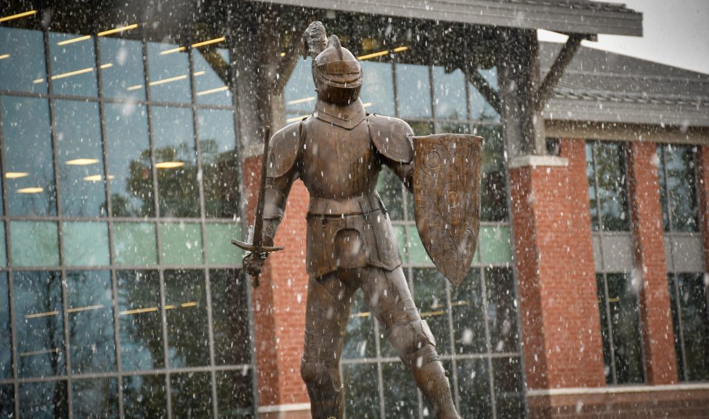 Snow flies around a statue of a knight. 