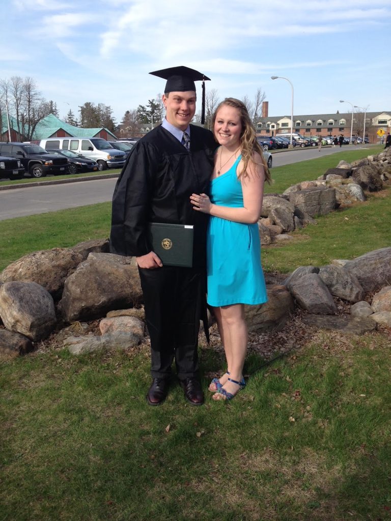 Alex Nicols in Graduation regalia standing with his wife