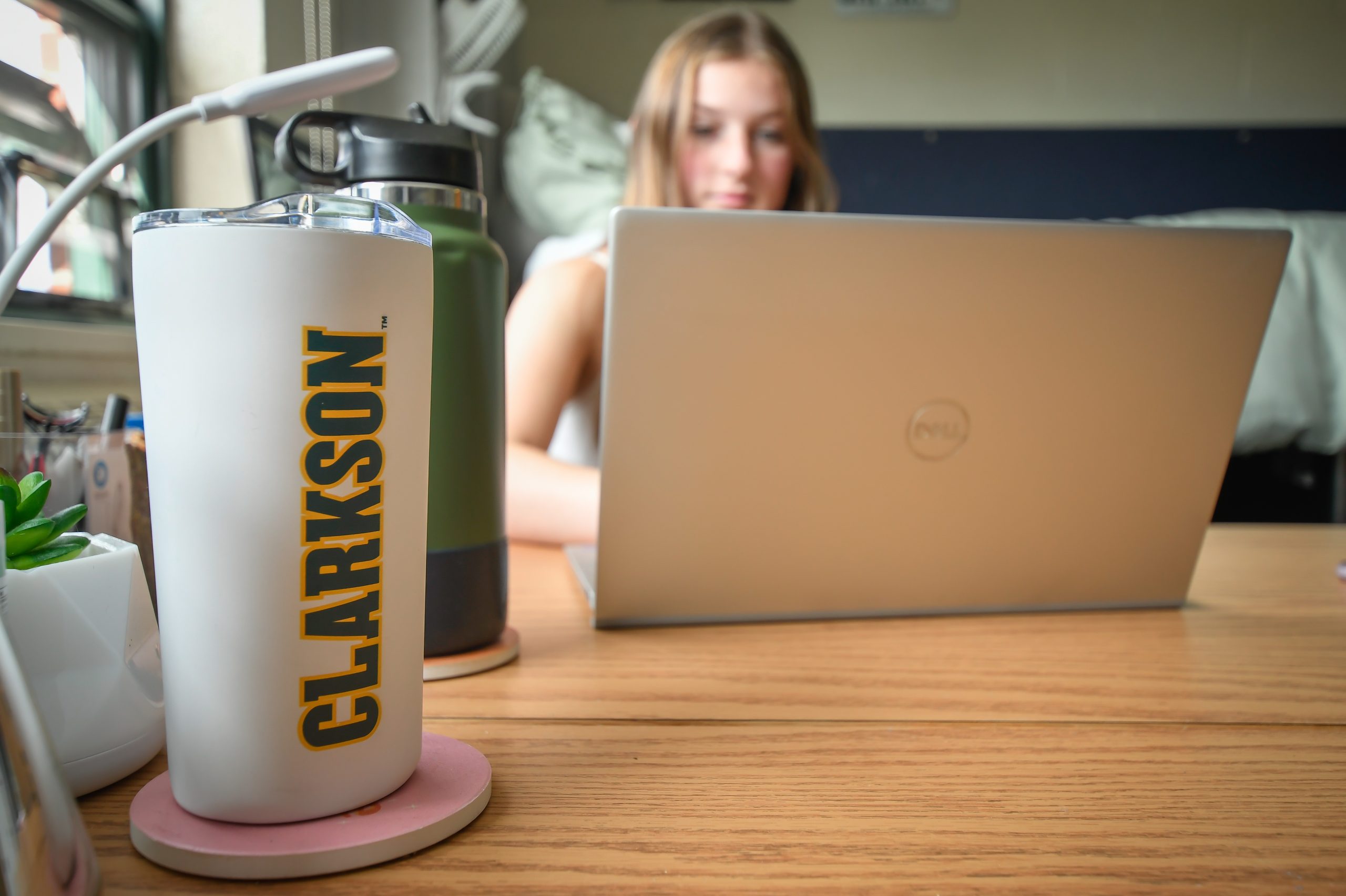 A women sitting behind a laptop screen with a Clarkson white tumbler in the foreground