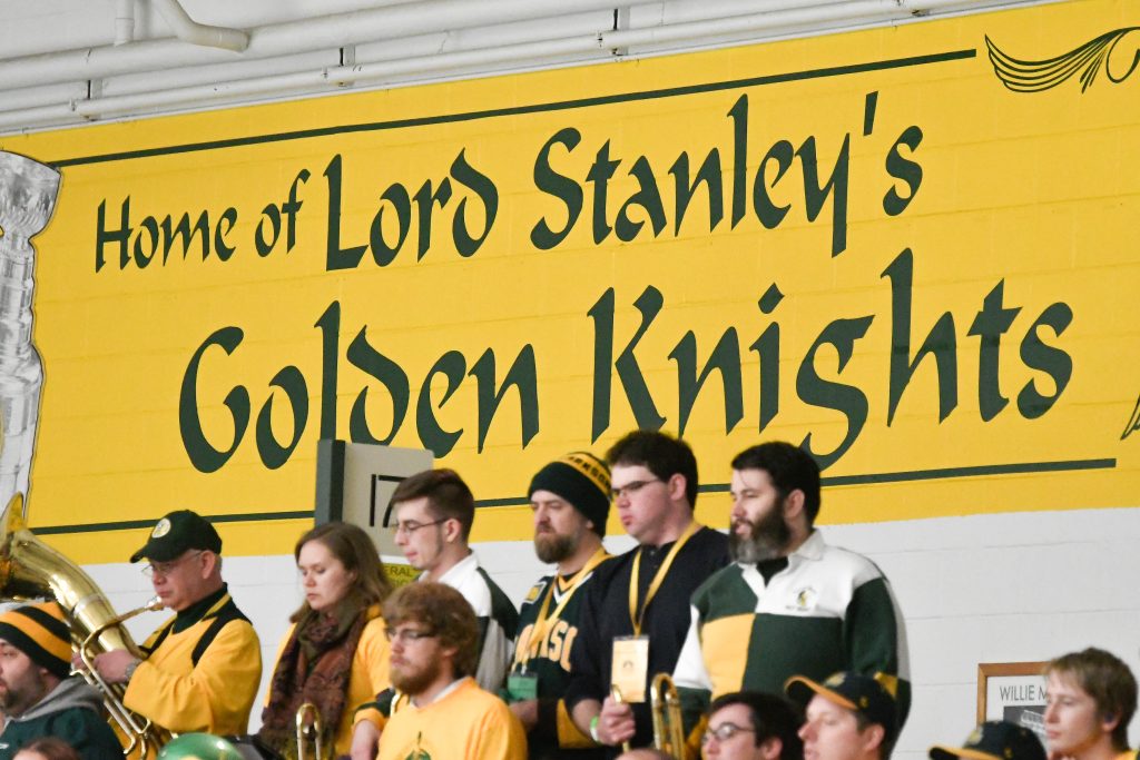 Students in the Clarkson University Pep Band standing in front of a Wall mural reading 'Home of Lord Stanley's Golden Knights'