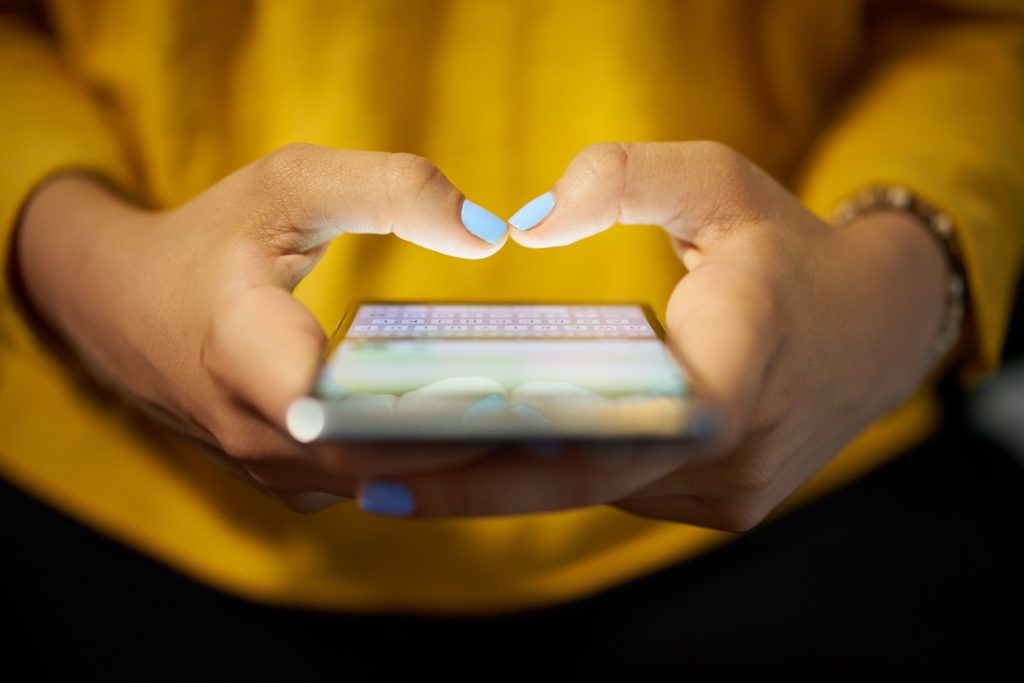 a women's hands that are holding a cellphone making a heart shape with her thumbs