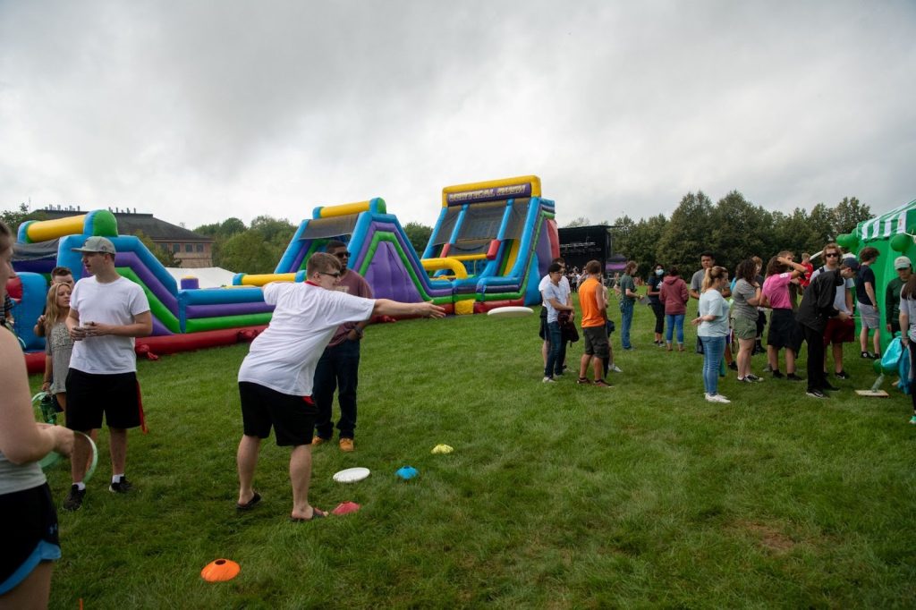 A crowd of people playing a frizz-by game with a bouncy setup in the background