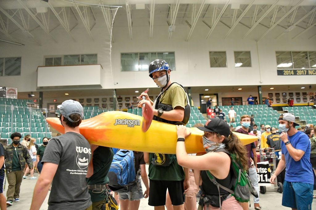 A group of students holding up a paddler in a canoe while walking through the arena floor