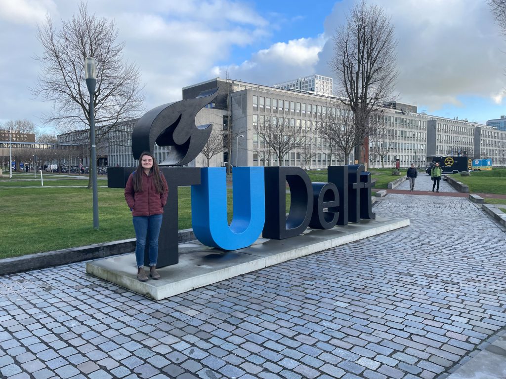 Person standing next to a letter statue that says T U Delft