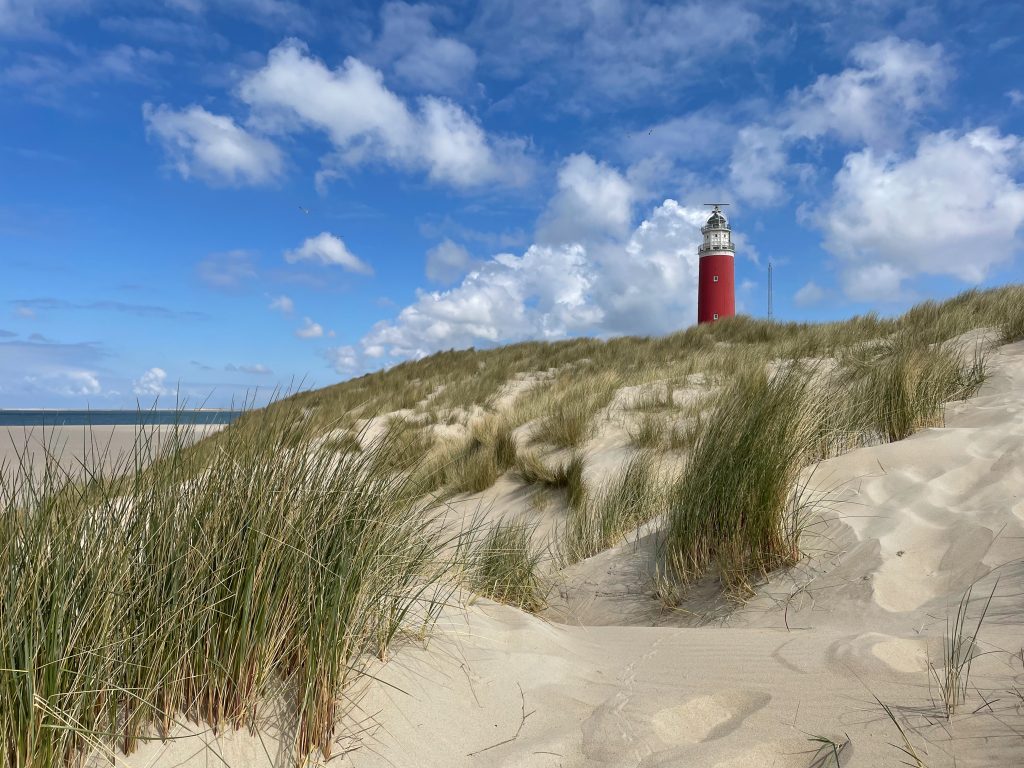 A red and white lighthouse sitting on top of a sandy beach dun that also has long strains of green grass growing