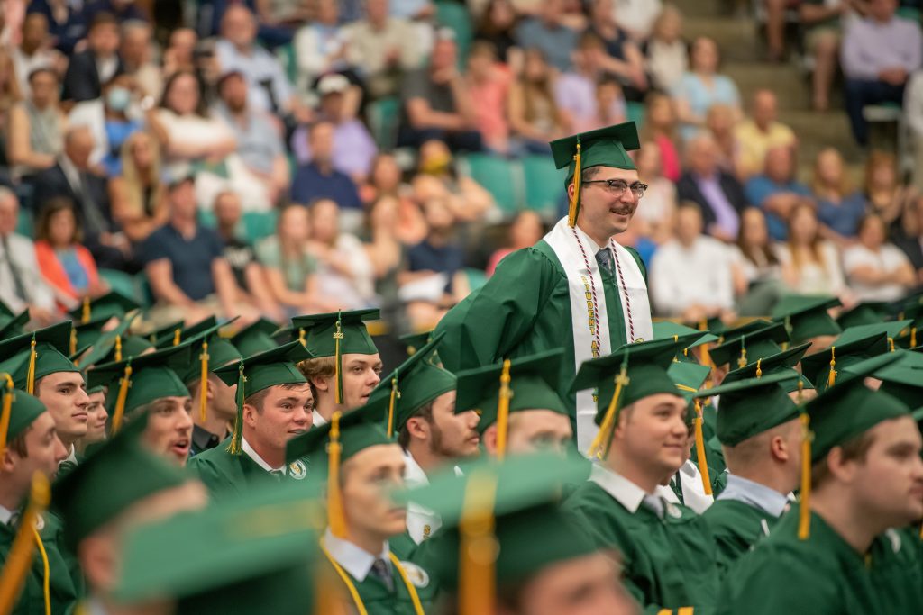 A man standing up in a sea of green graduates