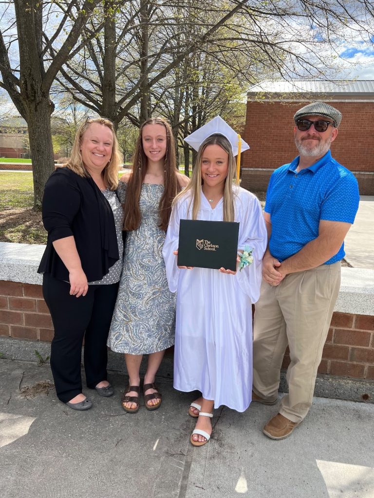Carly standing with her family. A family photo of 4 people while Carly holds her TCS diploma 