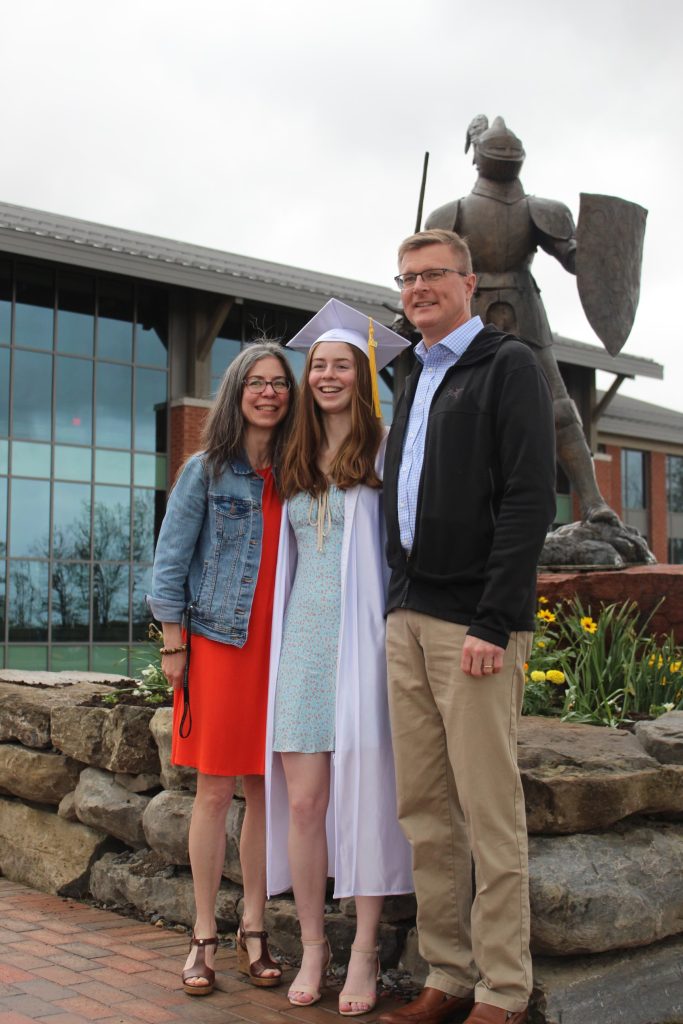 Sarah Jane standing in her The Clarkson School graduation gear with her parents next to the Golden Knight statue 
