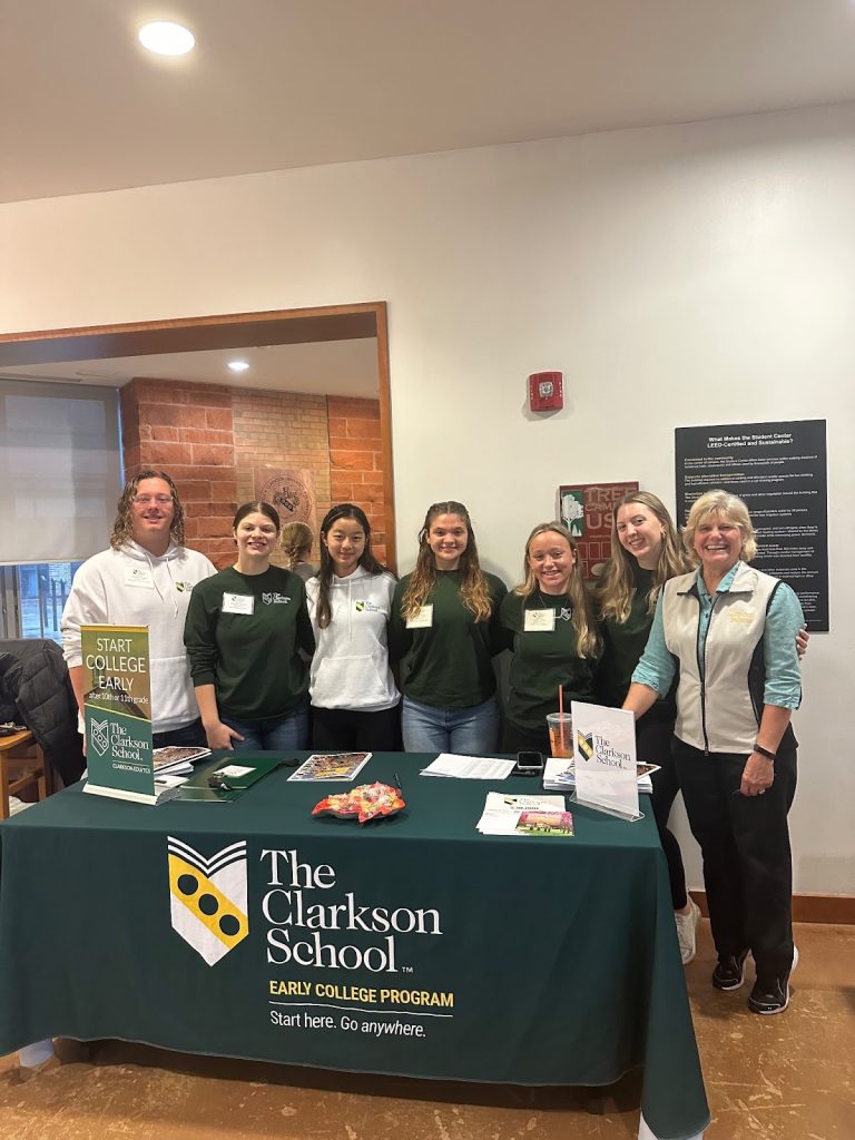 A group of 7 individuals standing behind the The Clarkson School table in the Student Center