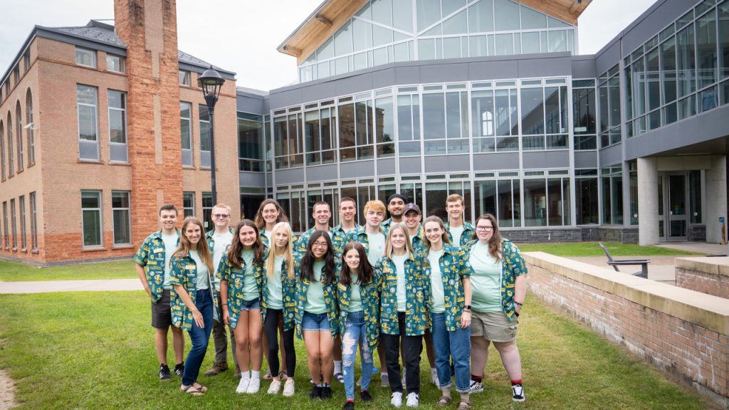 Members of the Office of Student Life staff, clad in green and gold Clarkson gear, pose for a photo by the Student Center. 