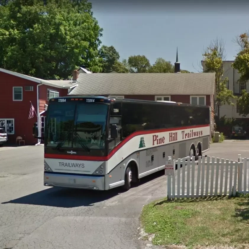 Large bus with red and white detail arrives in parking lot of station. Trailways buses offer a great option to international students traveling to Potsdam.