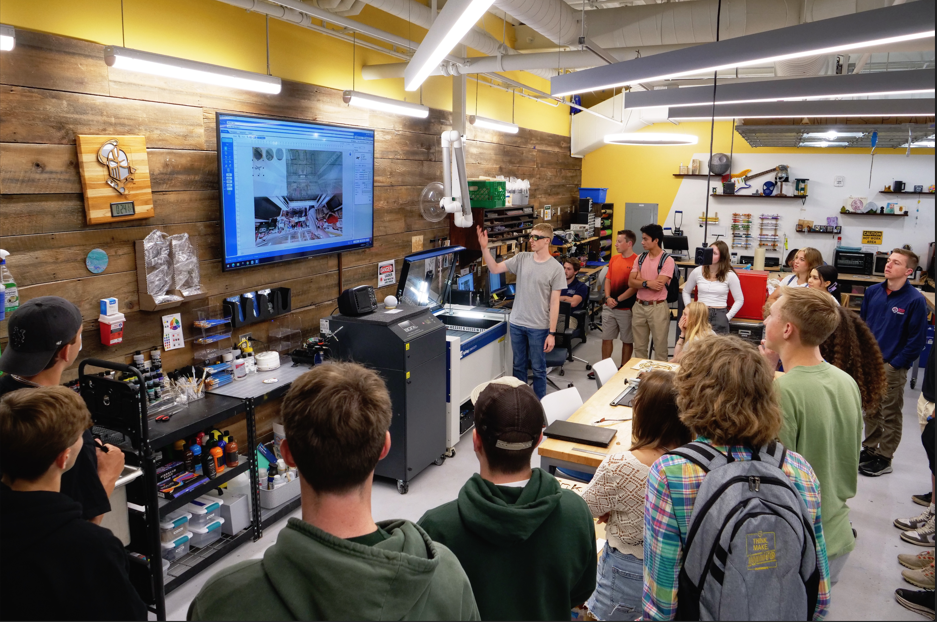 A group of students stand while listening to a presentation in the Dorf Makerspace.
