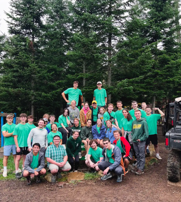 A group of students, wearing green t-shirts, smile and stand together.