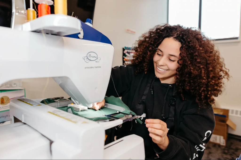 A female student smiles while using a sewing machine in the Makers’ Loft.