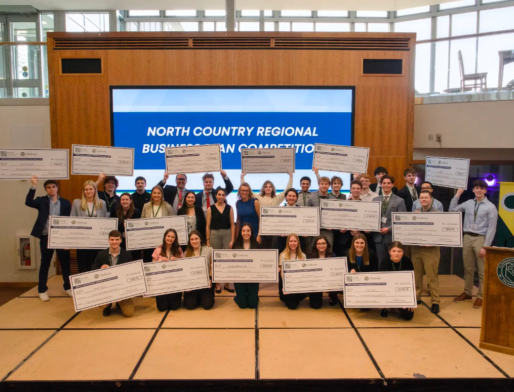 A group of students stand together while smiling, each holding a large check in the air.